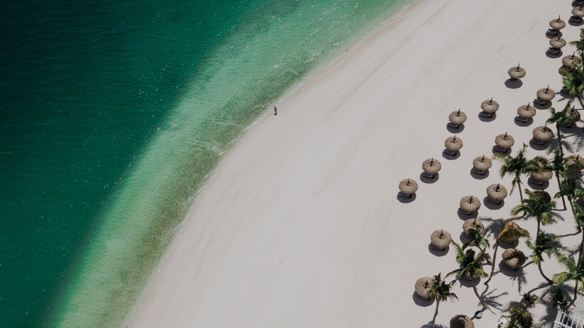 Ariel view of Mauritius' best white sandy beaches with crystal turquoise ocean. With sunbed and umbrella views. Visited during our South Africa Mauritius Holiday.