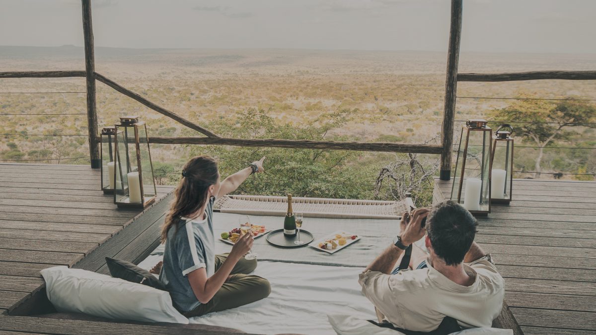 Couple enjoying a romantic meal and panoramic views from a cozy terrace setup during their honeymoon in Tanzania.