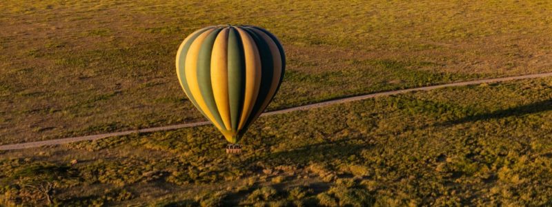 Green and yellow hot air balloon flying over the Serengeti National Park, in Tanzania.