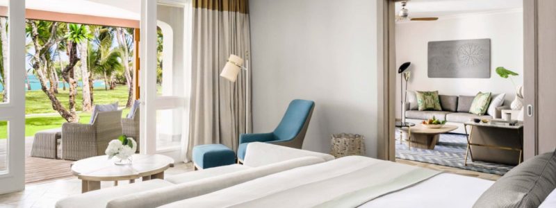 A bright and spacious Ocean Room at One&Only Le Saint Géran, featuring a comfortable bed, a seating area, and large sliding glass doors that open directly onto a private patio and tropical gardens, providing direct access to the resort's lush surroundings and views towards the lagoon.