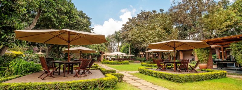 Lush gardens with shaded seating areas at Arusha Coffee Lodge, perfect for relaxing before a luxury safari in Tanzania.