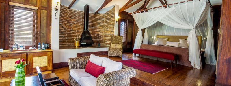 Elegant suite at Arusha Coffee Lodge with a canopied bed, cozy sitting area, and exposed wooden beams—ideal for a luxury safari stay in Tanzania.