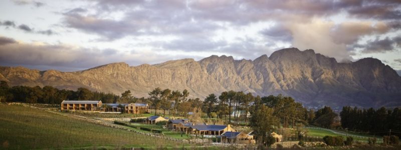 La Residence luxury estate set among vineyards, olive trees, and orchards in Franschhoek, with mountain views under a dramatic sky.