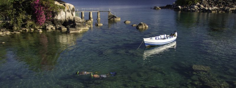 Kaya Mawa Snorkeling in scenic Malawi waters surrounded by purple and green vegetation. Luxury African safari.