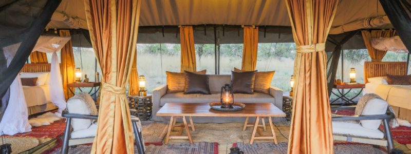 Luxurious interior of a safari tent featuring a cozy seating area, plush bedding, and lanterns at Legendary Expeditions in Tanzania.