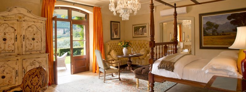 Elegant four-poster bed in the Honeysuckle Bedroom at La Residence, with chandeliers, antique furnishings, and vineyard views.