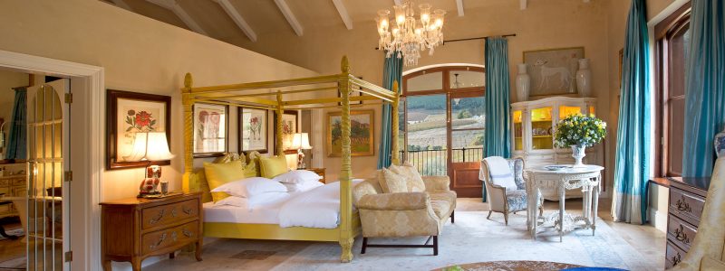 Elegant four-poster bed in the Honeysuckle Bedroom at La Residence, with chandeliers, antique furnishings, and vineyard views.