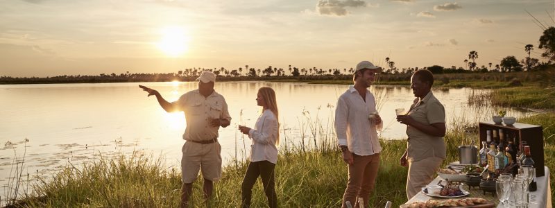 Sanctuary Retreats - Baines' Camp, Okavango Delta, Botswana. Couple romantic view of African landscape. With condiments refreshments and drinks. Talking to tour guides.