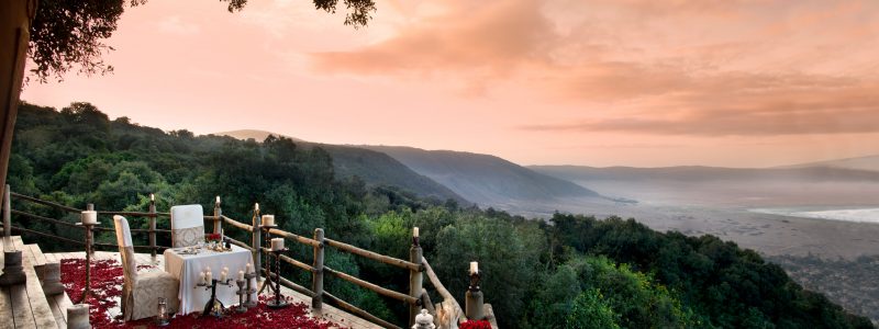 Elegant outdoor dining setup with rose petals and candlelight overlooking the Ngorongoro Crater in Tanzania at sunset.