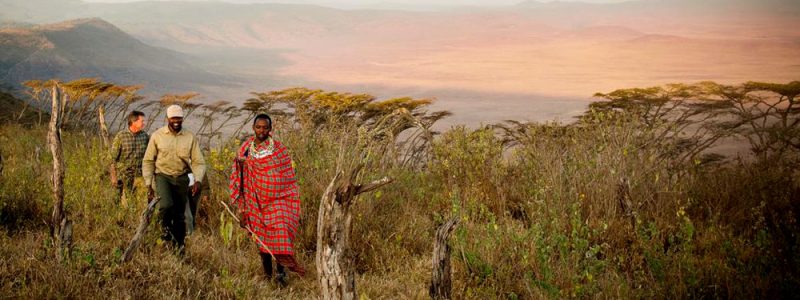 Three people, including a Maasai guide in traditional attire, walking through the Ngorongoro Highlands in Tanzania.