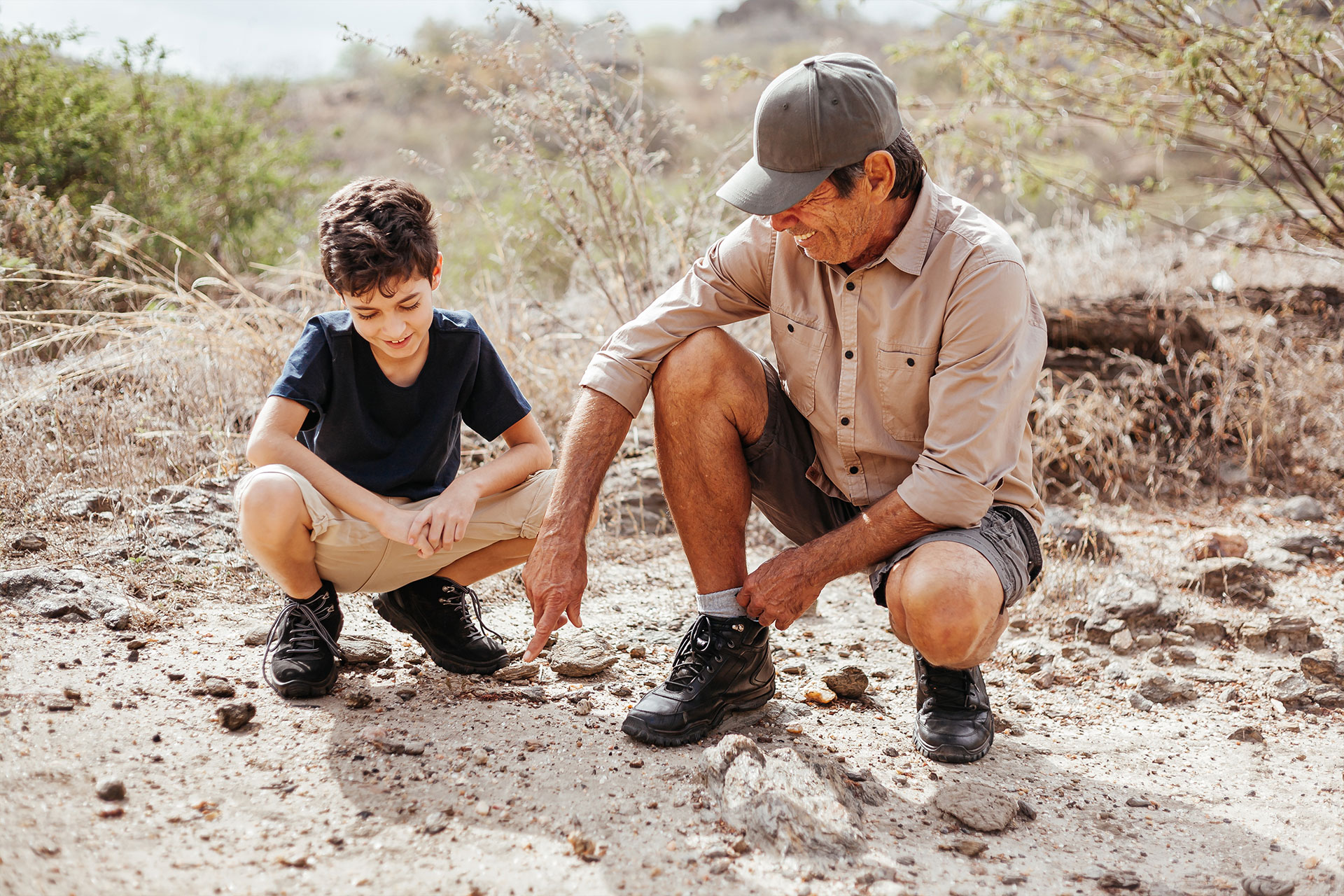 Father and son are exploring animal tracks on a multigenerational luxury safari in Africa.