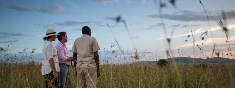 Luxury Kenya Safari Tourists and tour guide observing African sunset over mountains, from plains of Kenya.