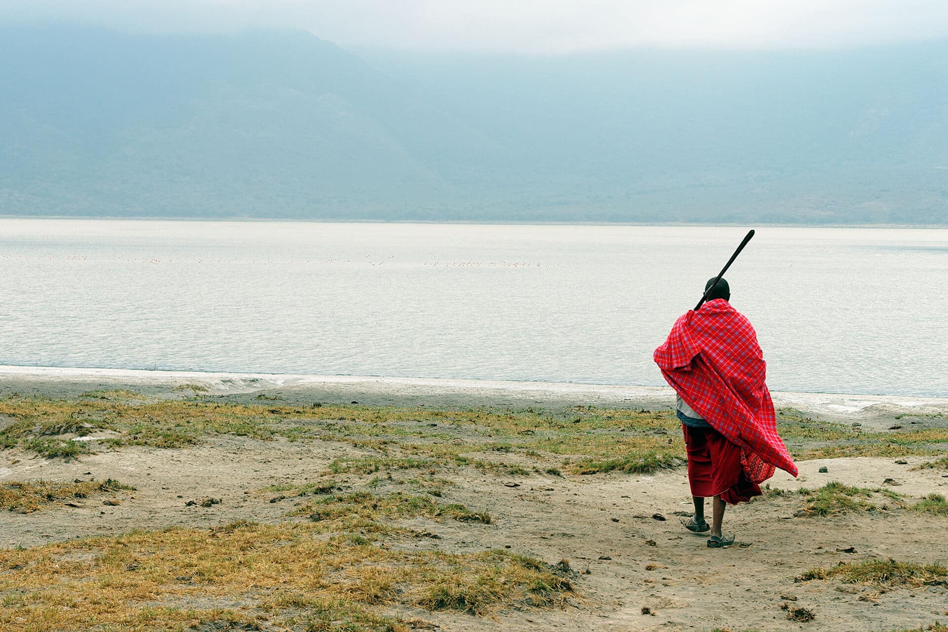 A solo traveler in traditional Maasai attire walking along a serene African lakeshore, symbolising cultural immersion and personal discovery on a solo safari adventure.