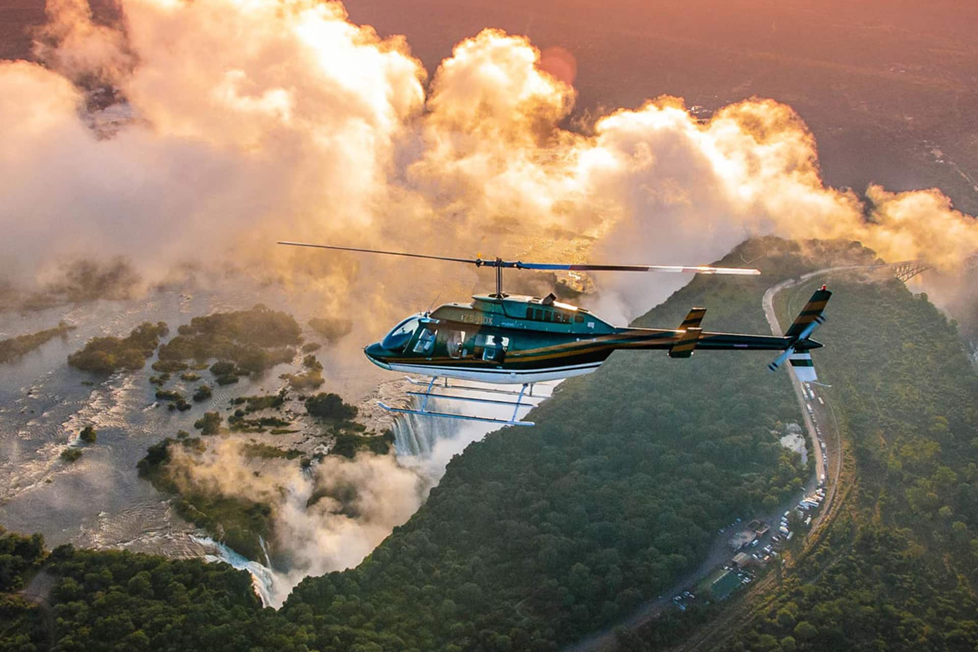 Helicopter flying over Victoria Falls at sunrise, surrounded by mist and dramatic skies, offering an unforgettable bucket list safari adventure in Africa.