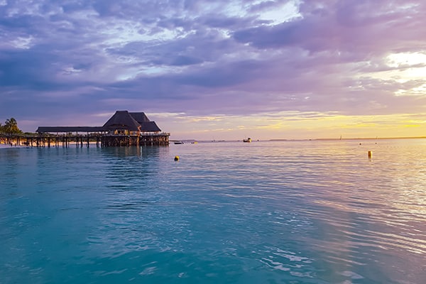 Beautful sunset and purple skies above light blue African seas. With villa and beach areas of Zanzibar in the background.