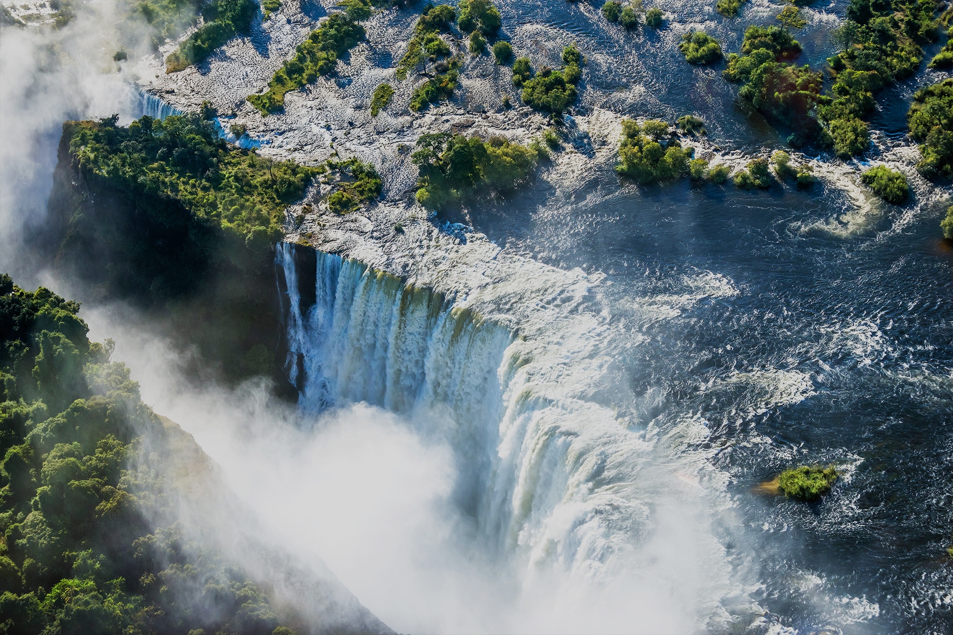 Aerial view of Victoria Falls surrounded by lush greenery and mist, showcasing the natural beauty of Zimbabwe's safari experience.