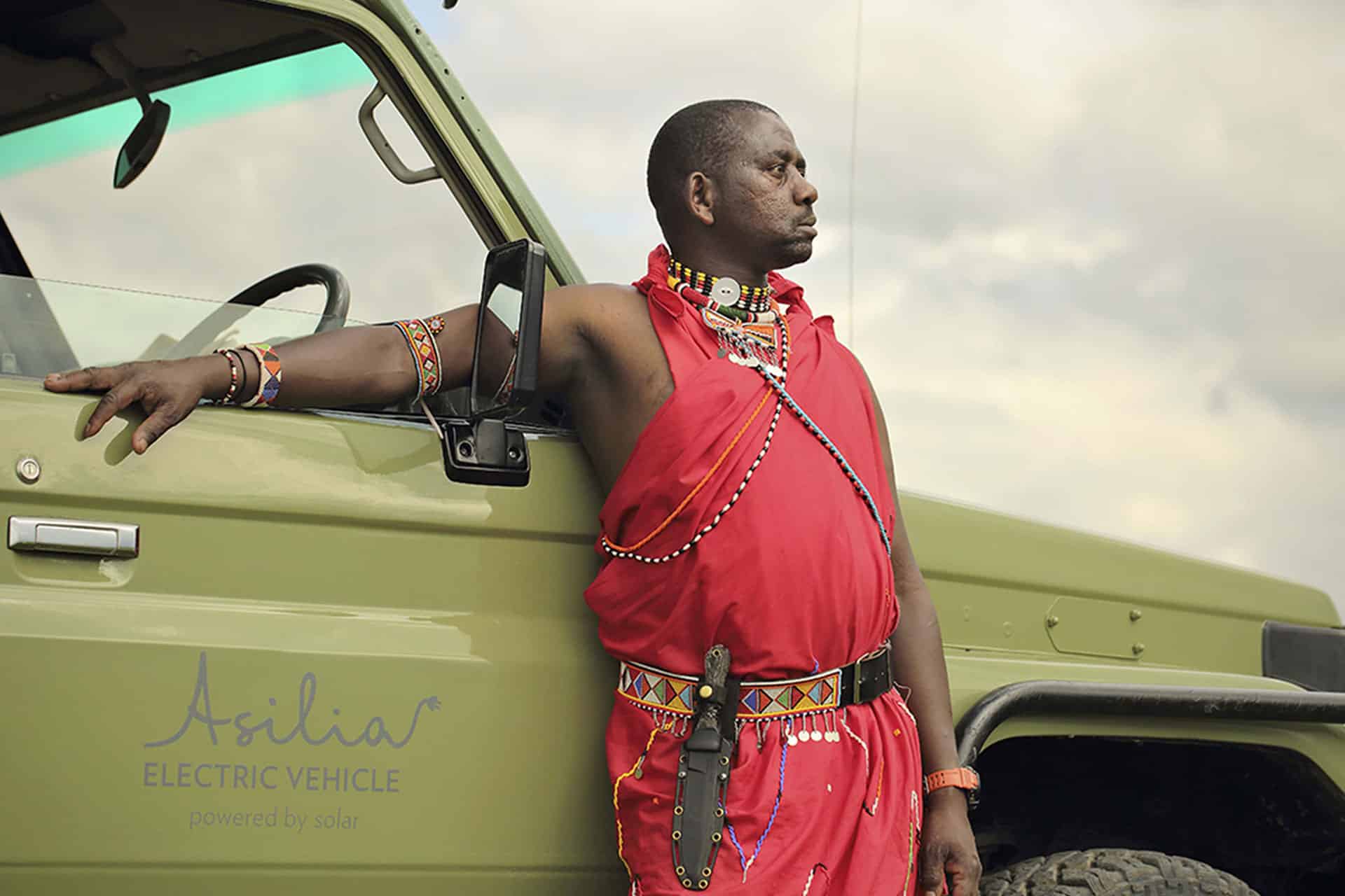 A Maasai guide leaning on an electric safari vehicle in Kenya 