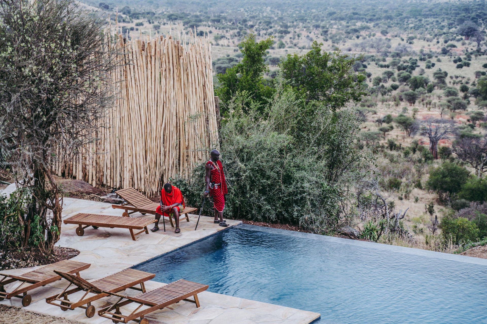 Two maasai men conversing around a swimming pool at Lemala Mpingo Ridge &ndash; a luxury lodge in East Africa. 