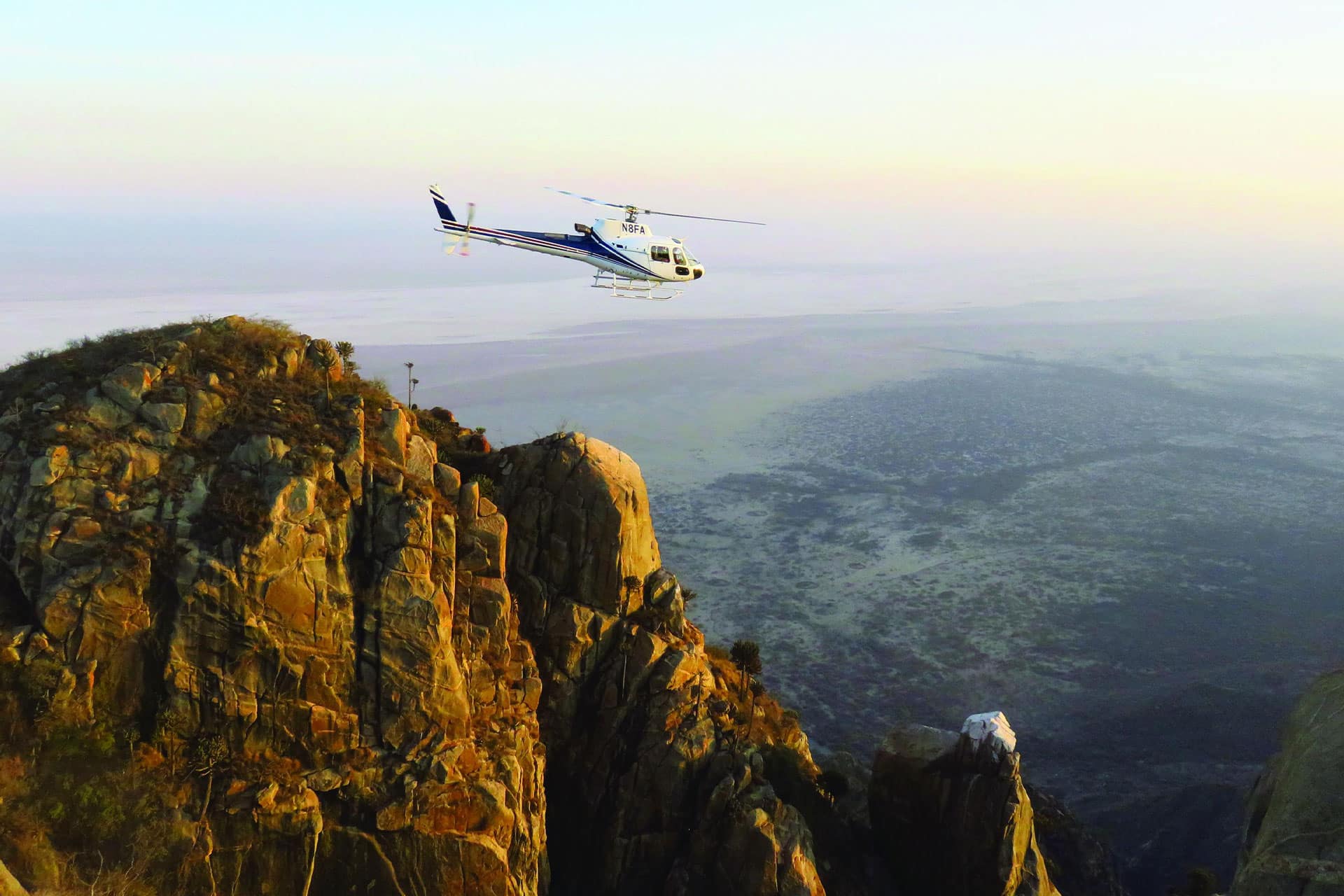 A helicopter from Mwiba Lodge flying over a mountain landscape.