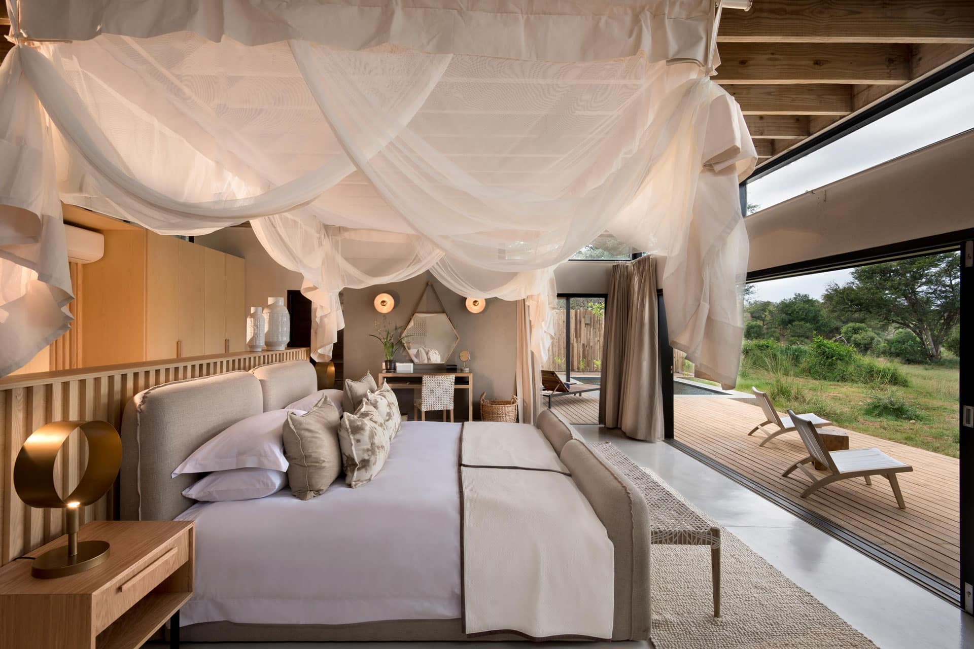 A luxury room with a large bed and open sliding doors looking out into the bush.