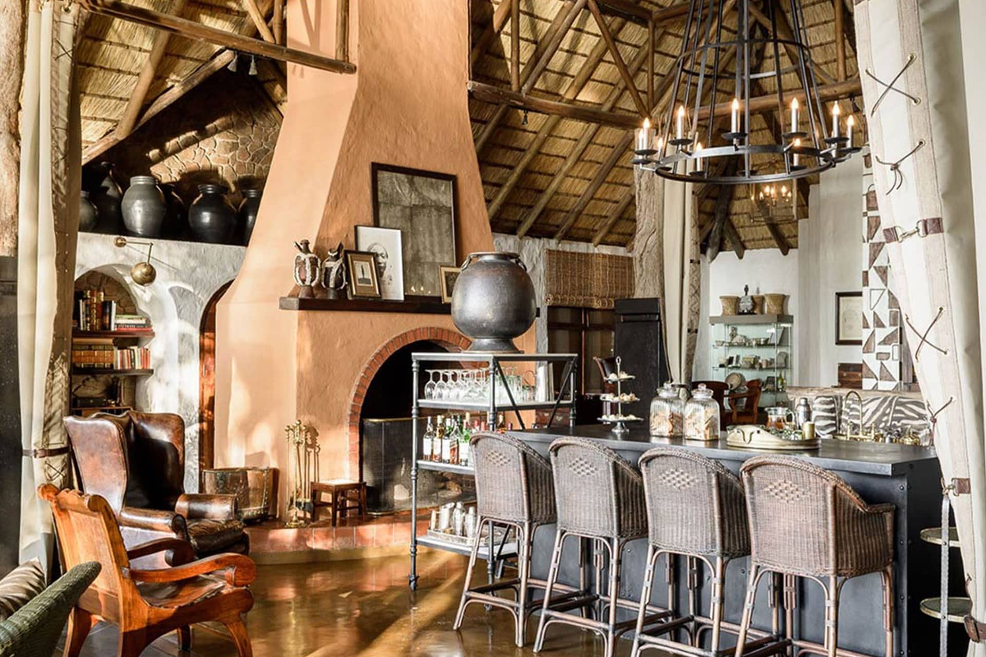 A seating area, bar and fireplace adorned with antique furniture and luxury finishes at Singita Sabi Sands Ebony Lodge.