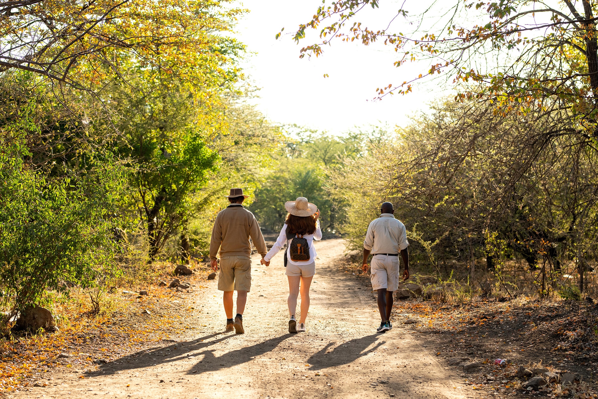 Couple holding hands on a guided walking safari through sunlit African bushveld, offering a romantic and adventurous honeymoon experience in the wild.