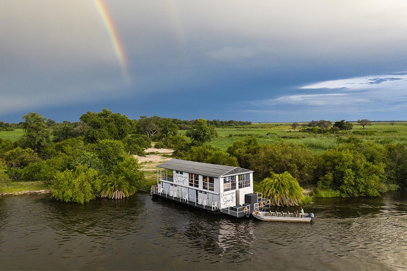 A luxurious houseboat moored on a serene African river, surrounded by lush greenery, offering an exclusive boat safari experience amidst stunning wildlife and landscapes.