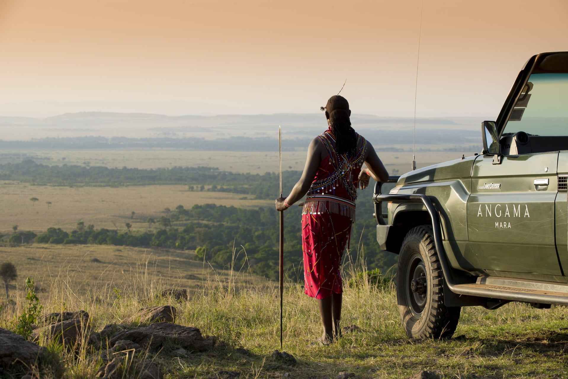 A Maasai warrior leaning on a game drive vehicle at Angama Mara&ndash; one of our top rated eco lodges in Africa. 