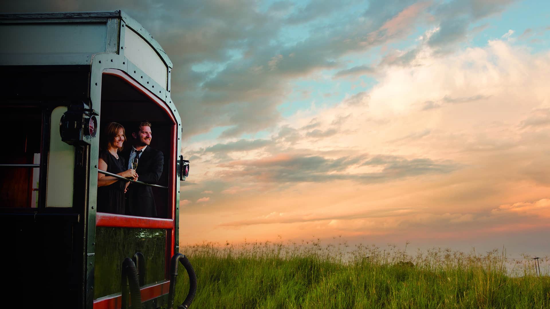 Couple enjoying the view from a luxury train carriage at sunset, capturing the romance and elegance of old-world travel across Africa&rsquo;s breathtaking landscapes.