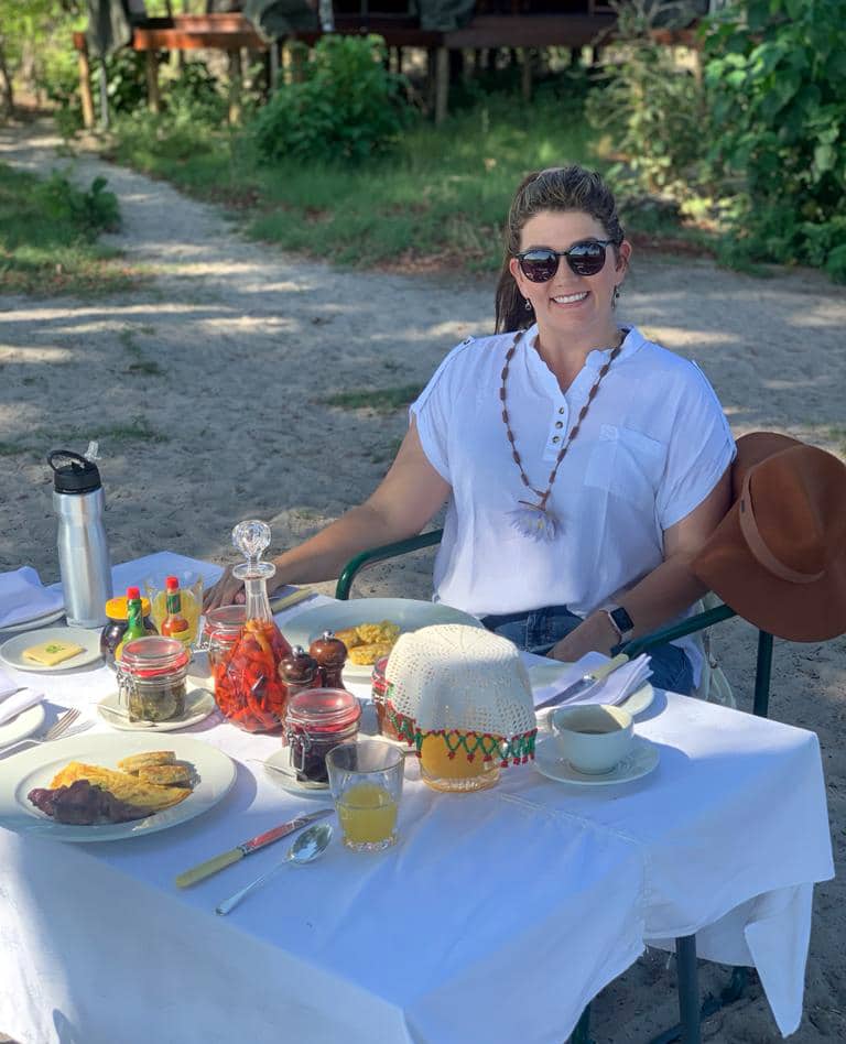 A woman sitting at a set table with food outside at Duke&rsquo;s Camp.
