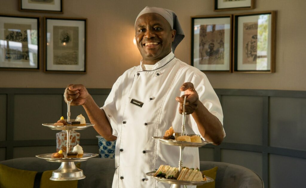 a smiling waiter serving high tea at Stanley & Livingstone Boutique Hotel
